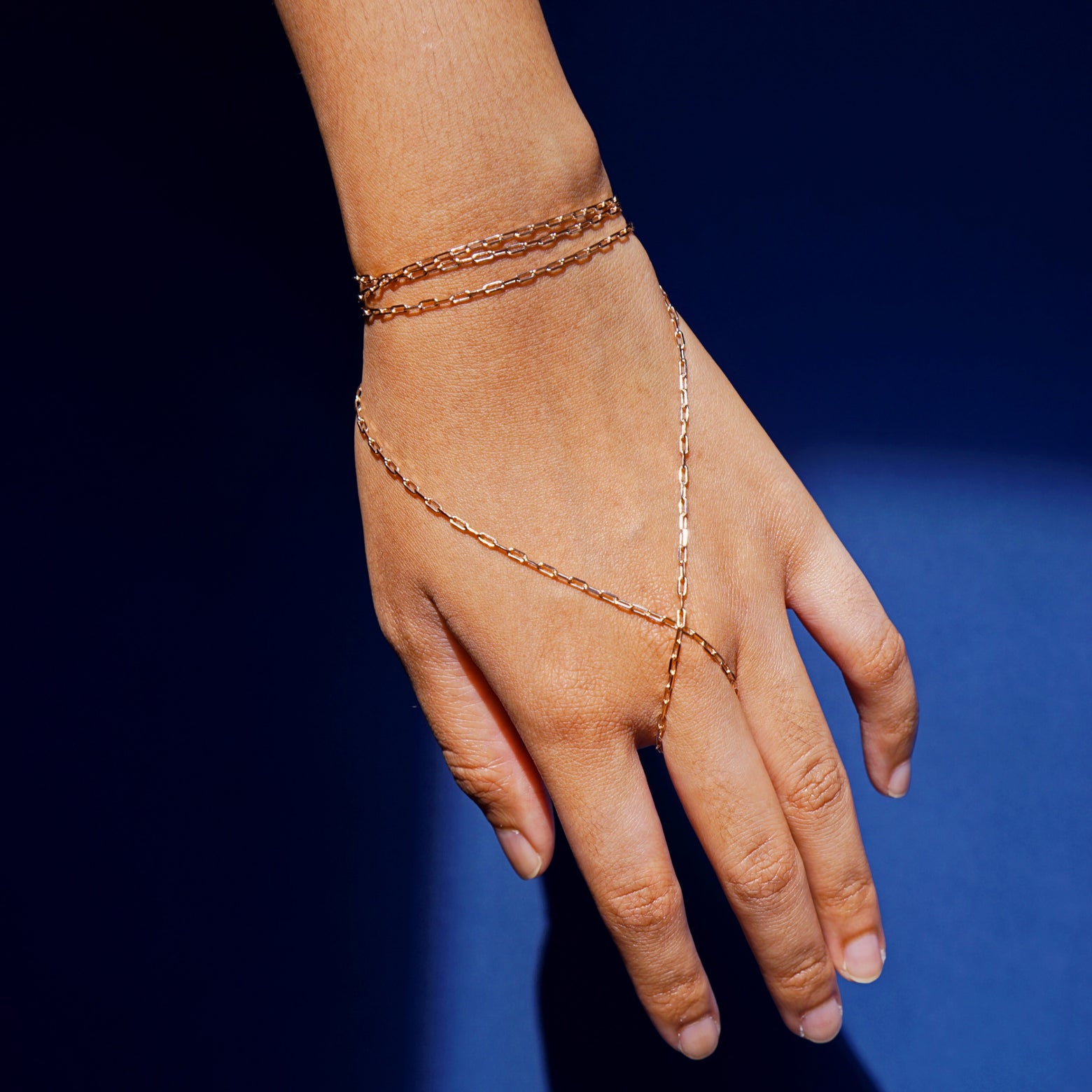 Close up view of a model wearing a 14k rose gold Wrap Necklace as a hand chain that wraps around their middle finger