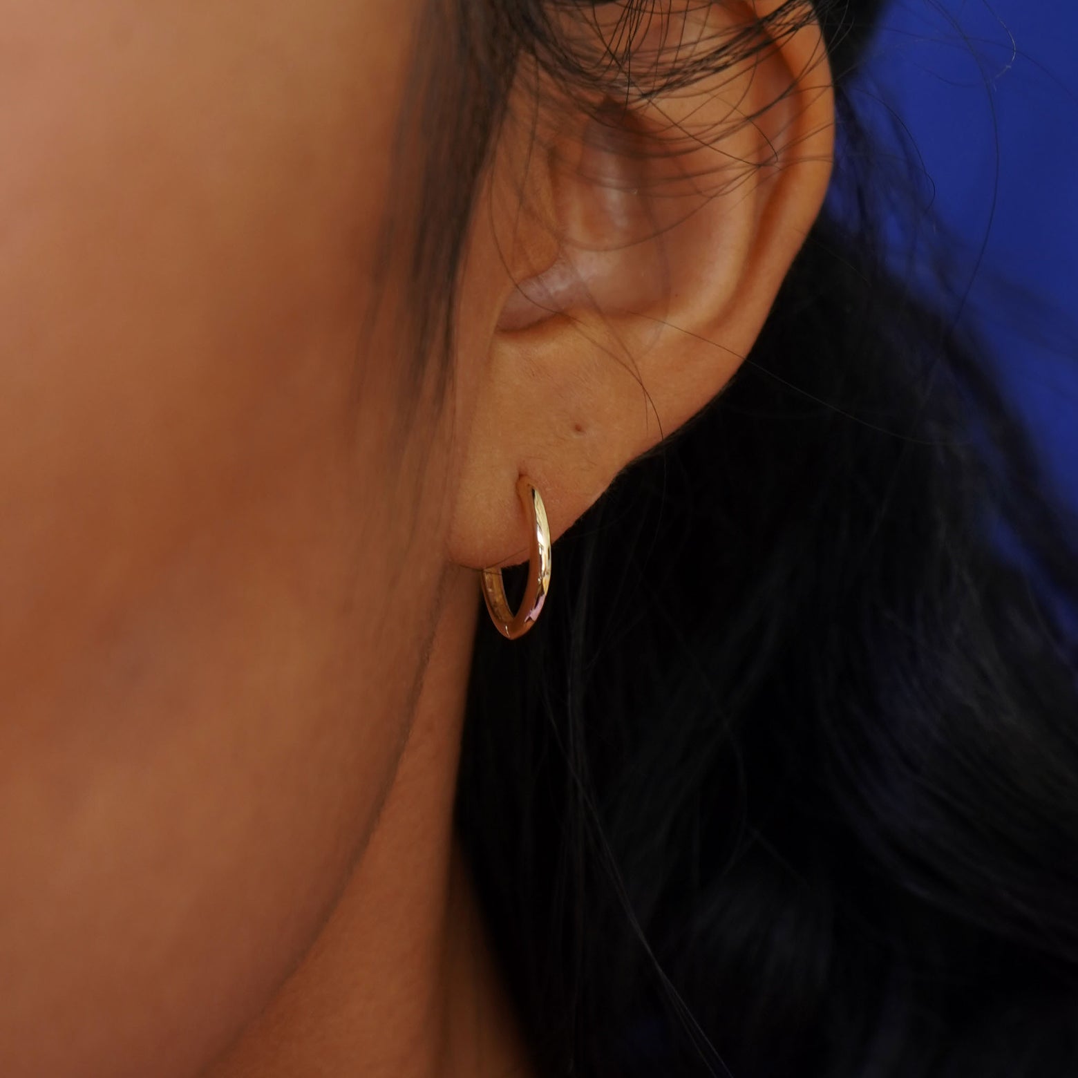 A model's ear wearing a 14k solid gold Medium Curvy Huggie Hoop