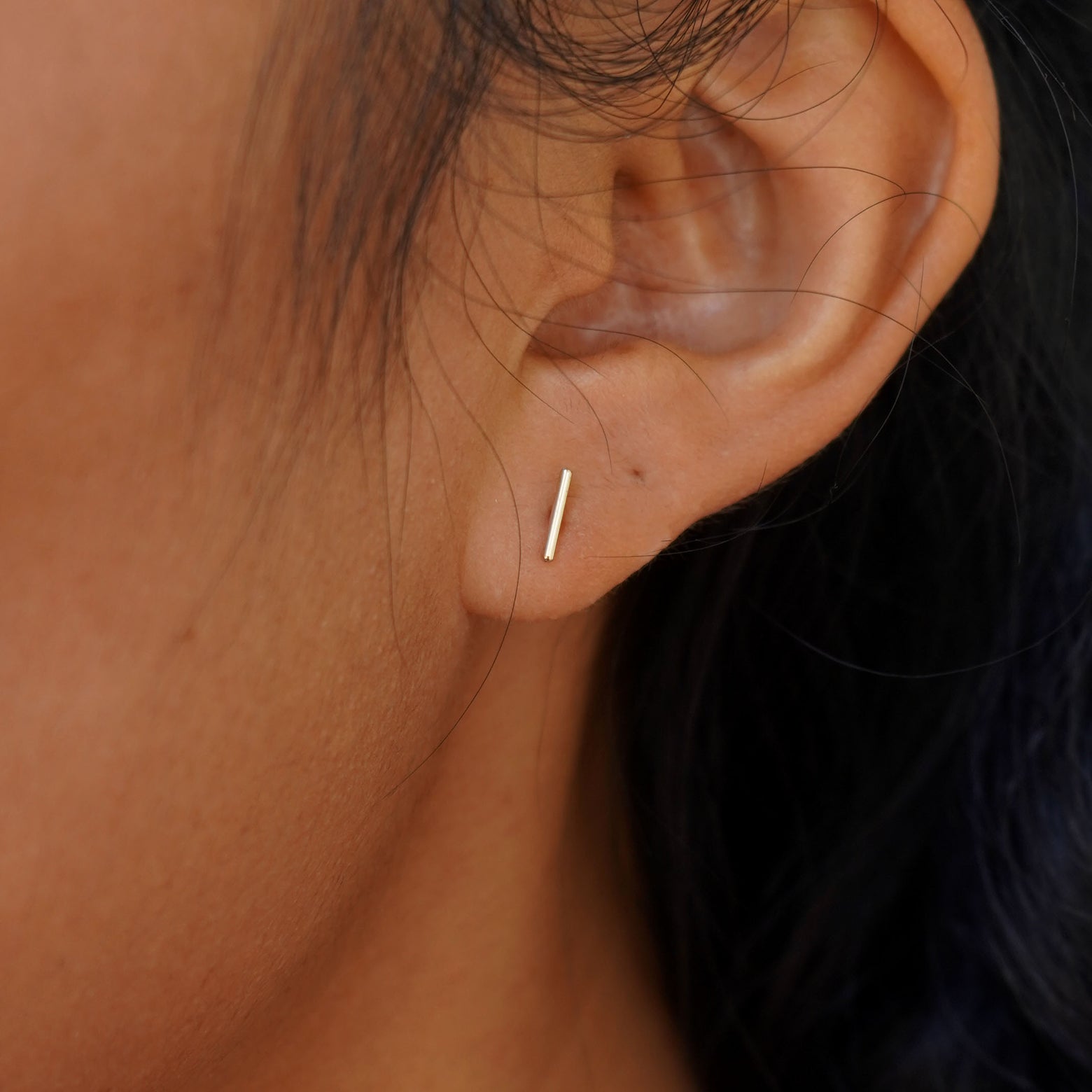 Close up view of a model's ear wearing a yellow gold Medium Line Earring