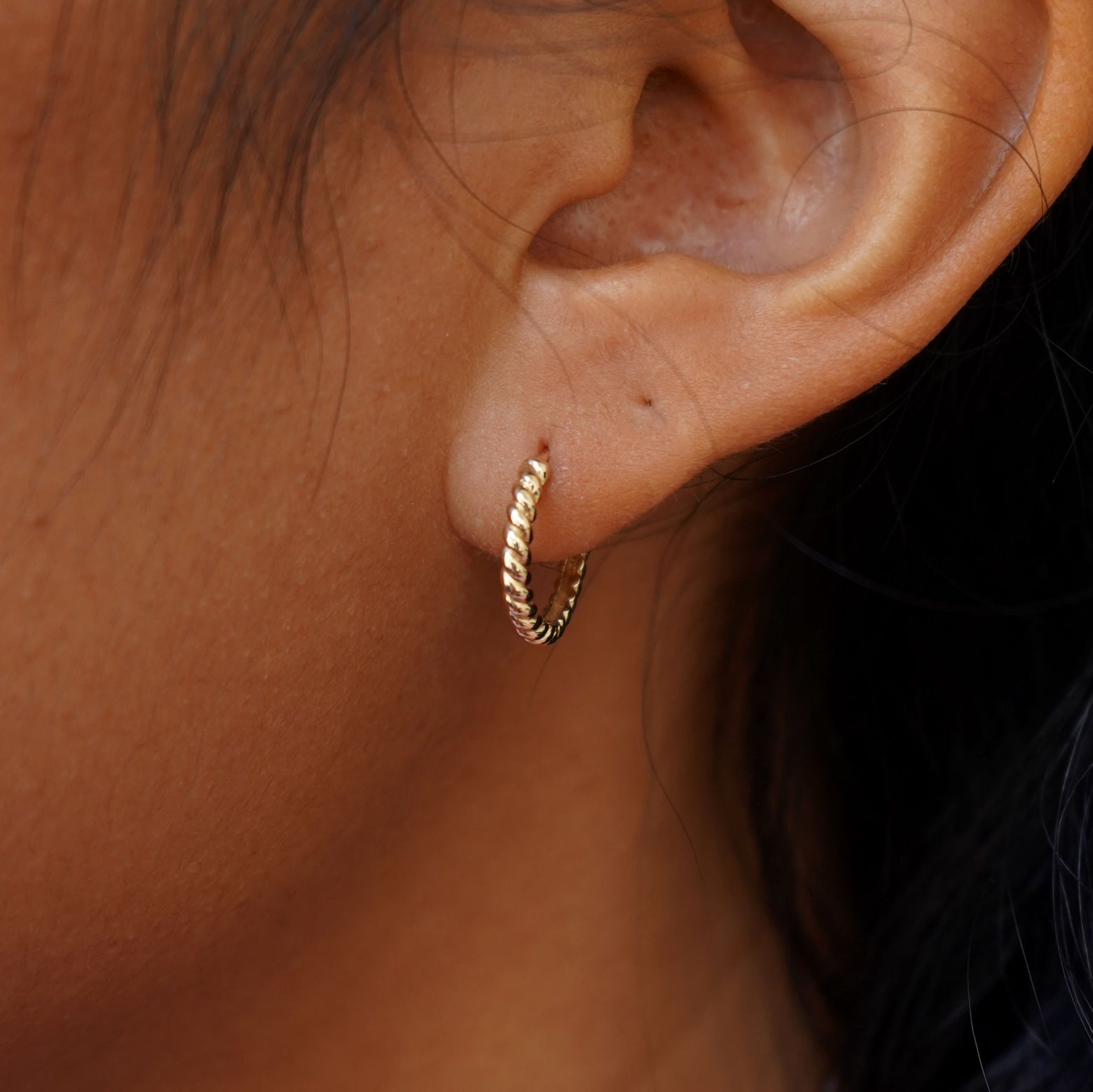 Close up view of a model's ear wearing a yellow gold Medium Rope Huggie Hoop