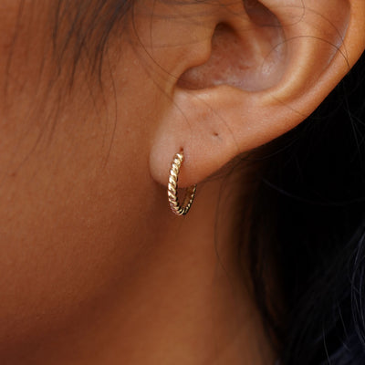 Close up view of a model's ear wearing a yellow gold Medium Rope Huggie Hoop