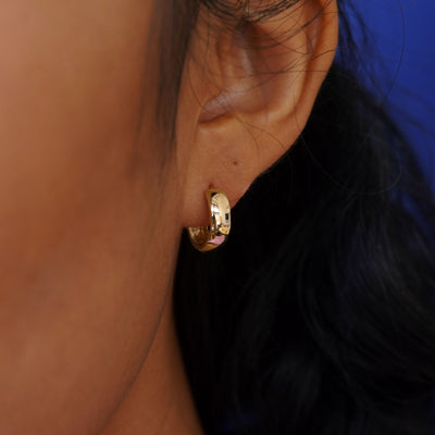 Close up view of a model's ear wearing a yellow gold Medium Thick Huggie Hoop