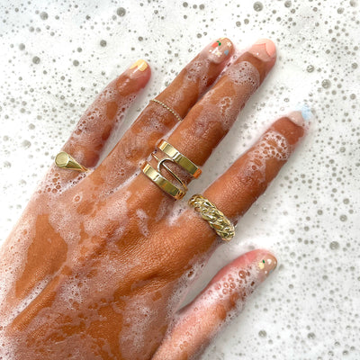 A model's hand in very soapy water wearing various Automic Gold rings