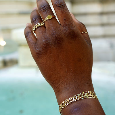 A model hand raised wearing a yellow gold Miami Cuban Ring, a Signet Ring, and a Wave Ring as well as several Butch Bracelets