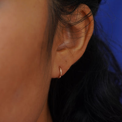 A model's ear wearing a solid gold Mini Curvy Huggie Hoop