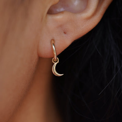 Close up view of a model's ear wearing a yellow gold Moon Charm on a Curvy Huggie Hoop