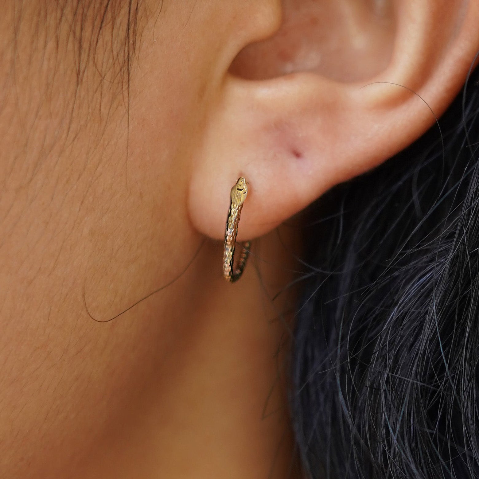 A model's ear wearing a 14k yellow gold Snake Hoop / Piercing