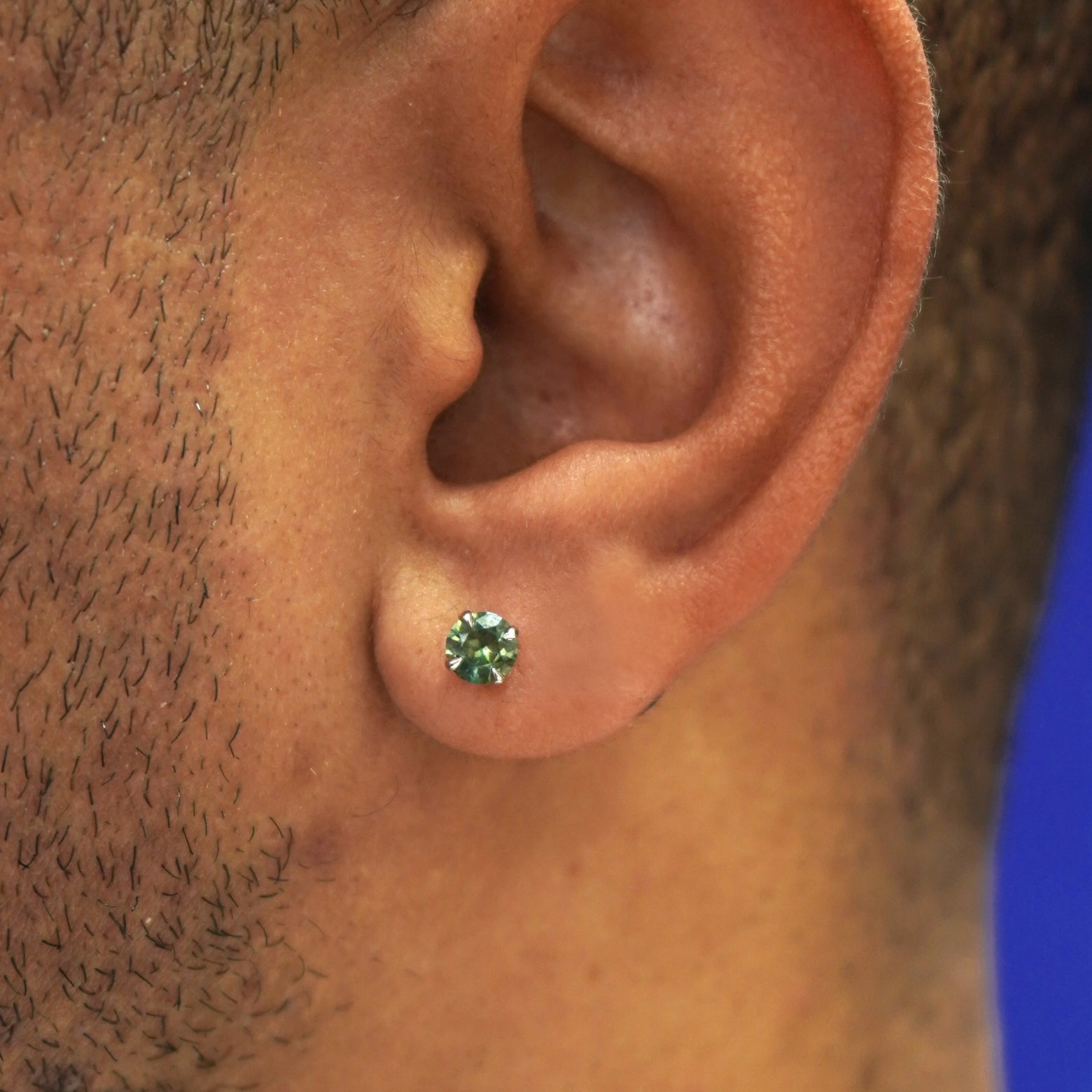 A model's ear wearing a solid 14k gold green sapphire pressure lock earring