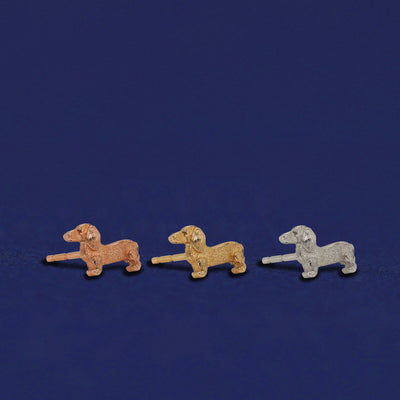 Three versions of the Dog Earrings shown in options of rose, yellow, and white gold