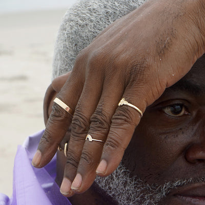 A model sitting on the beach with their hand across their head wearing a Rainbow Ring and other Automic Gold jewelry