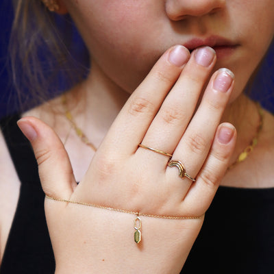 A child's hand wearing a Rainbow Ring and a Line Ring while holding an Essential Bracelet with a Tanlah Charm