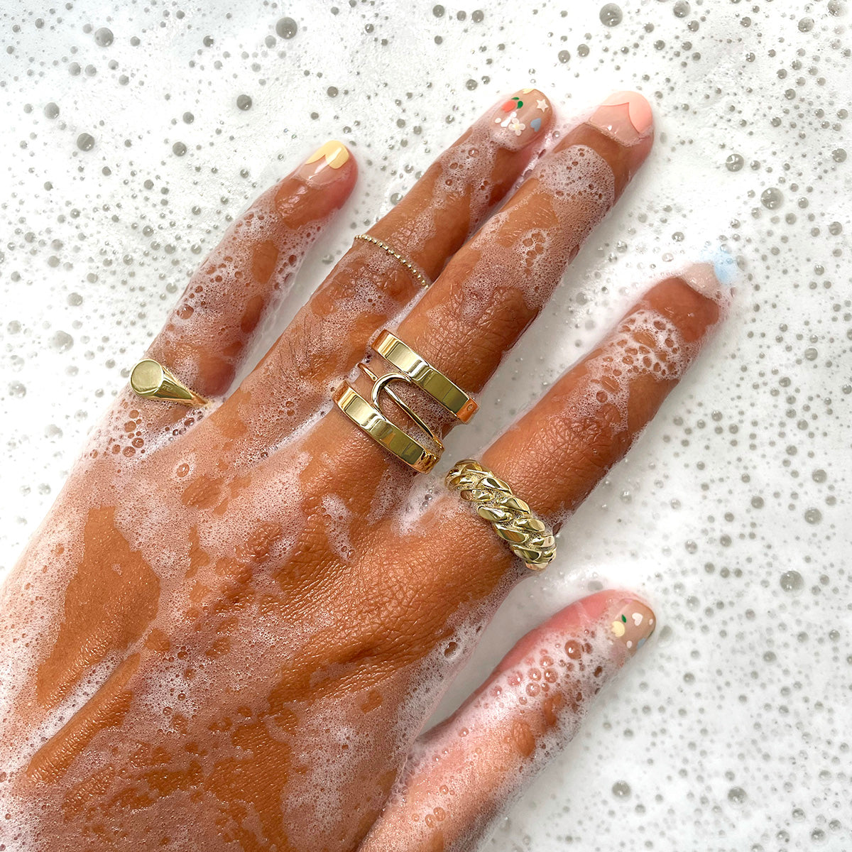 A model wearing various Automic Gold Rings sticking their hand into soapy water