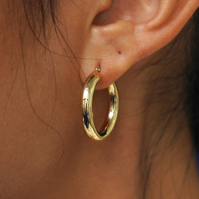 Close up view of a model's ear wearing a yellow gold Small Tube Hoop Earring