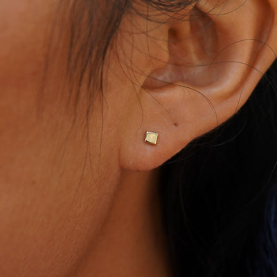 Close up view of a model's ear wearing a yellow gold Tiny Square Earring