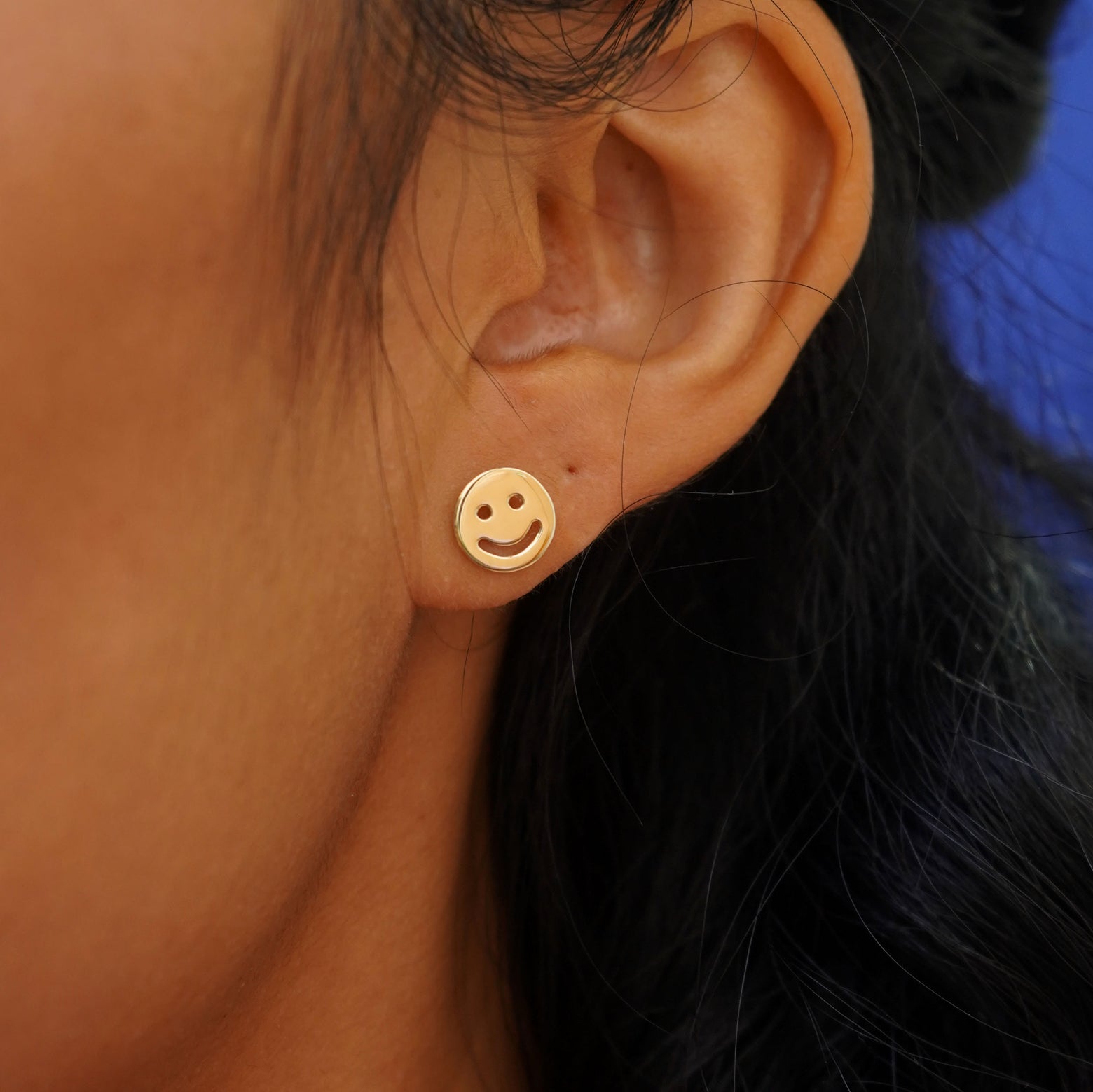 A model's ear wearing a 14k gold Smiley Face Earring