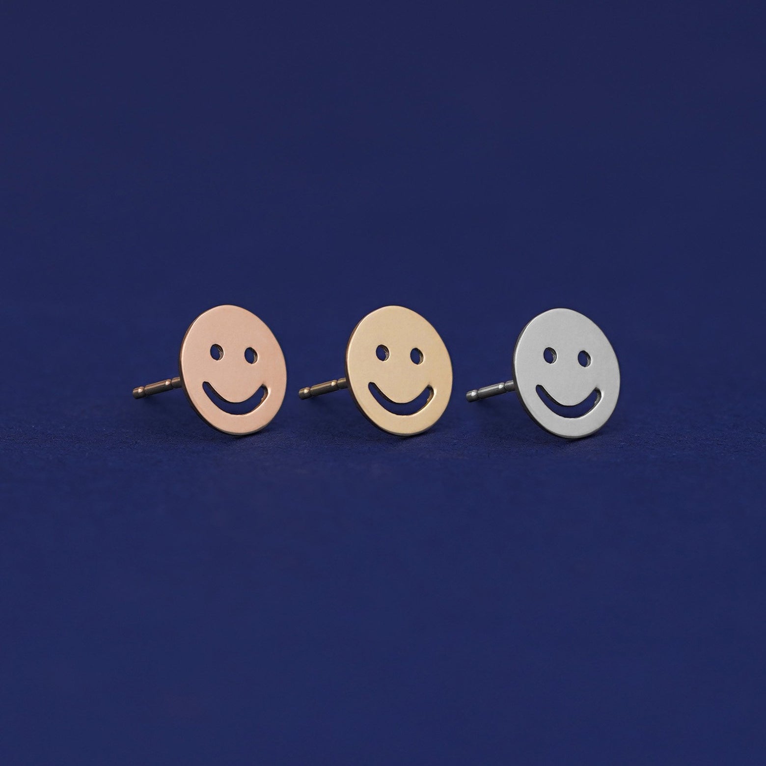 Three versions of a Smiley Face Earring shown in options of rose, yellow, and white gold