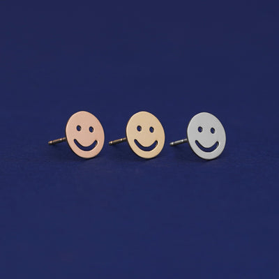 Three versions of a Smiley Face Earring shown in options of rose, yellow, and white gold