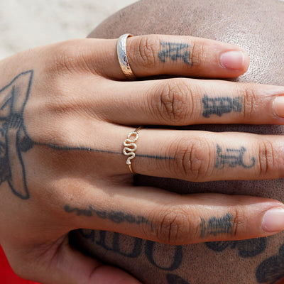 A tattooed model with their hand on the back of their head wearing a snake ring and a curvy mirror band