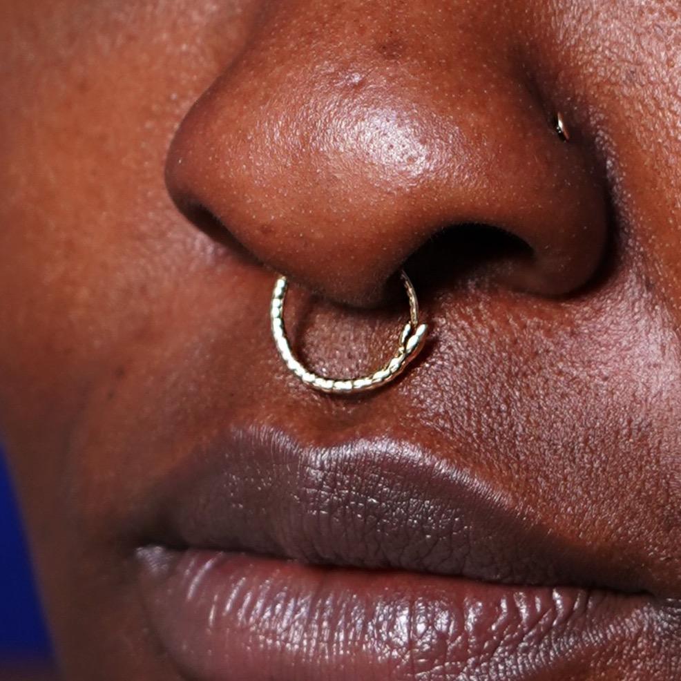 Close up view of a model's nose wearing a 14k yellow gold Snake Hoop / Piercing as a septum ring