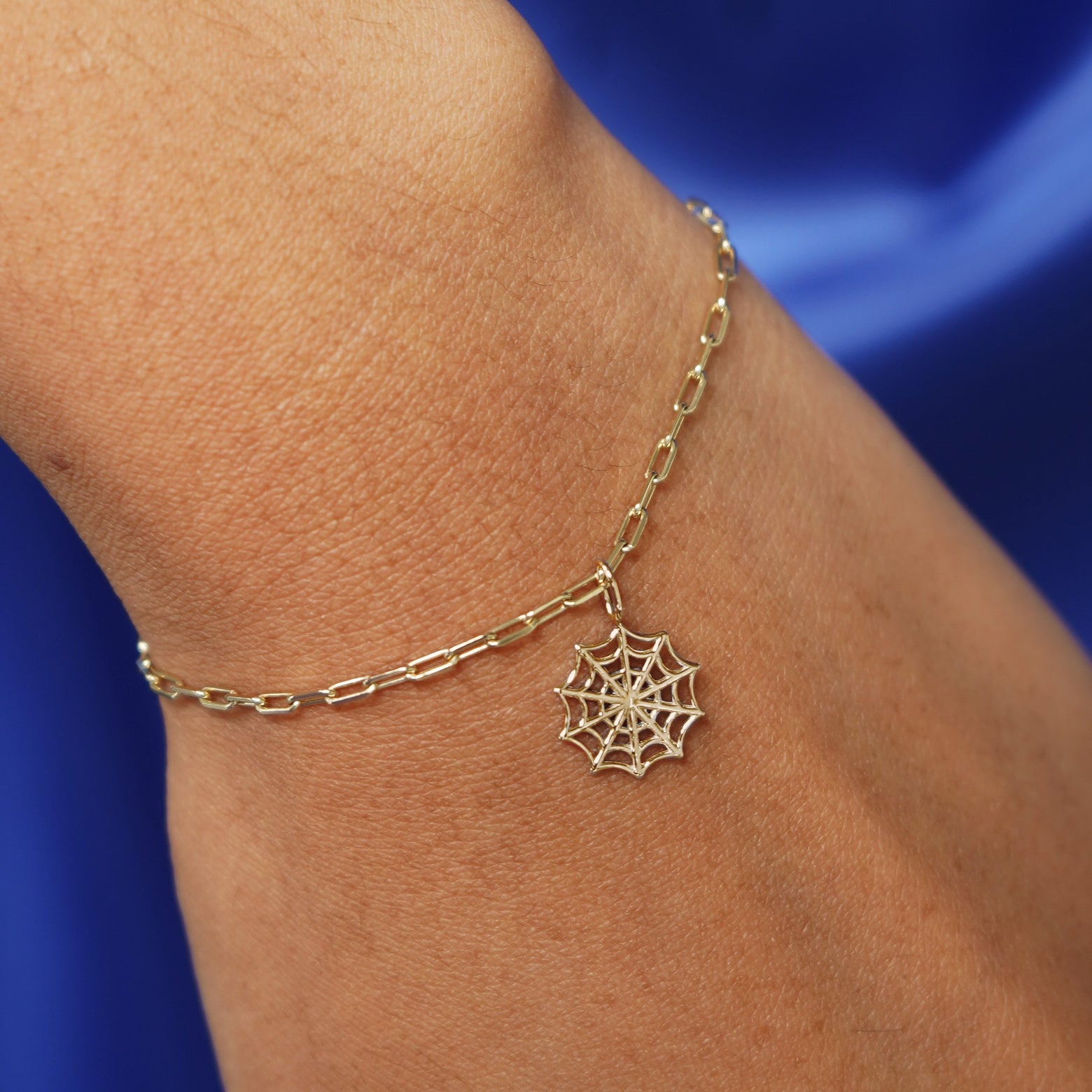 Close up view of a model's wrist wearing a yellow gold Spider Web Charm on a Butch Chain Bracelet