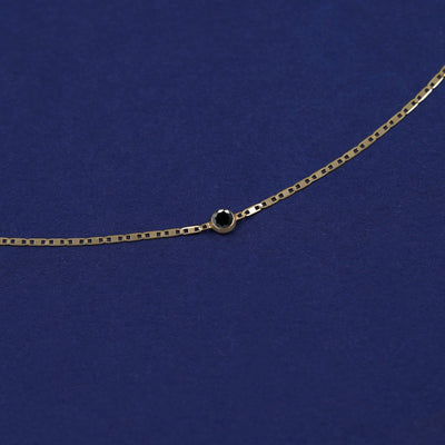 Bezel set 0.12ct Black Diamond solitaire on a 14 karat gold Valentine chain bracelet laid out on a dark blue background