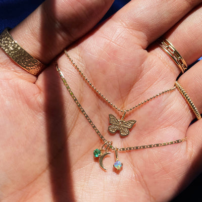 A model's hand holding two Automic Gold necklaces and wearing various yellow gold rings