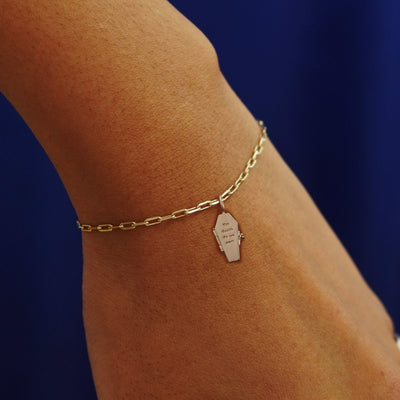 Close up view of a model's wrist wearing a yellow gold Coffin Charm on a Butch Bracelet