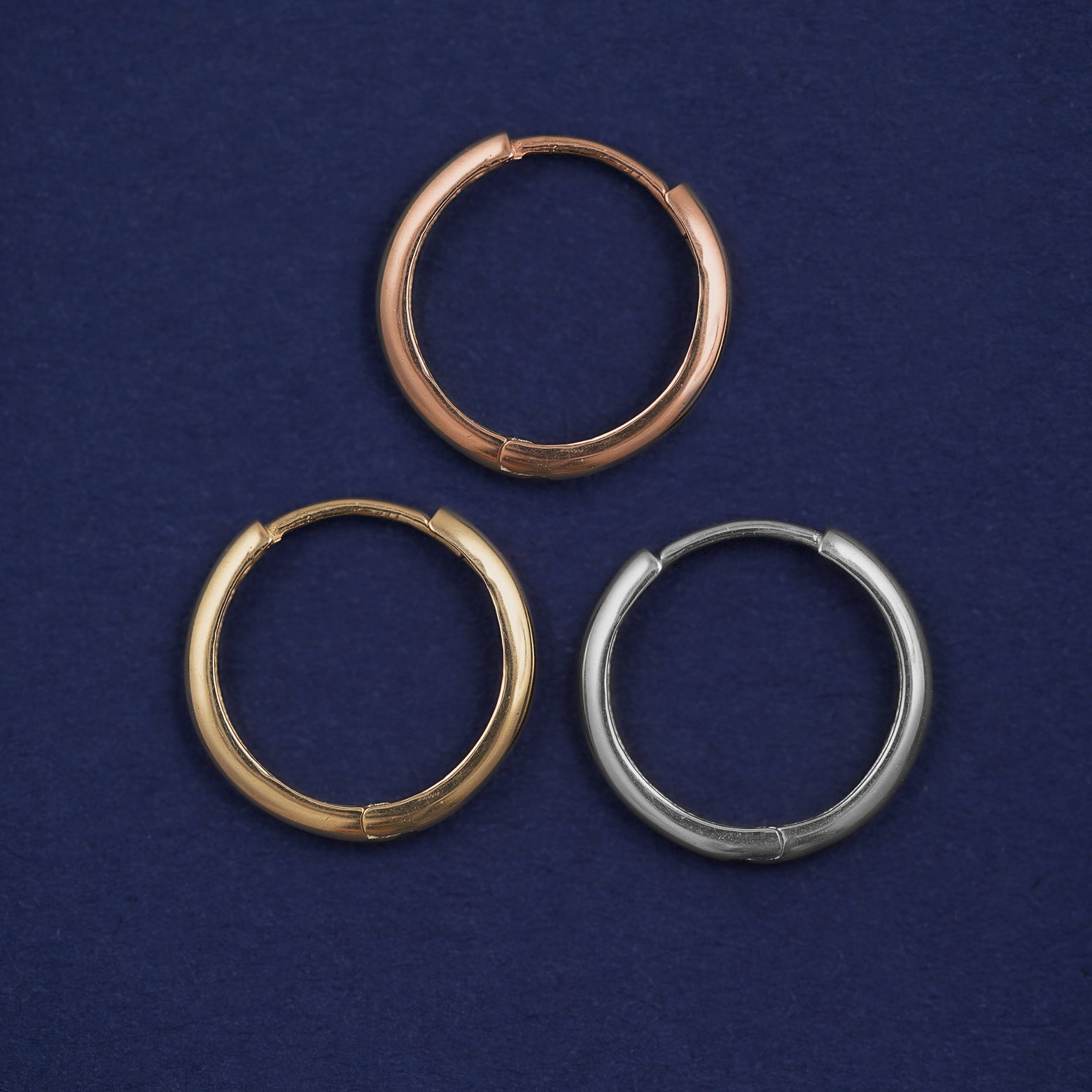 Three versions of the Medium Curvy Huggie Hoop shown in options of rose, yellow, and white gold