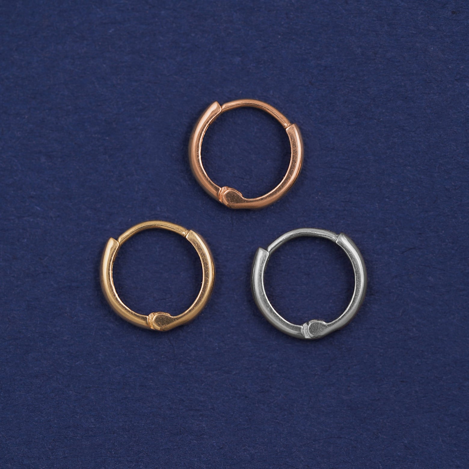 Three versions of the Mini Curvy Huggie Hoop shown in options of rose, yellow, and white gold