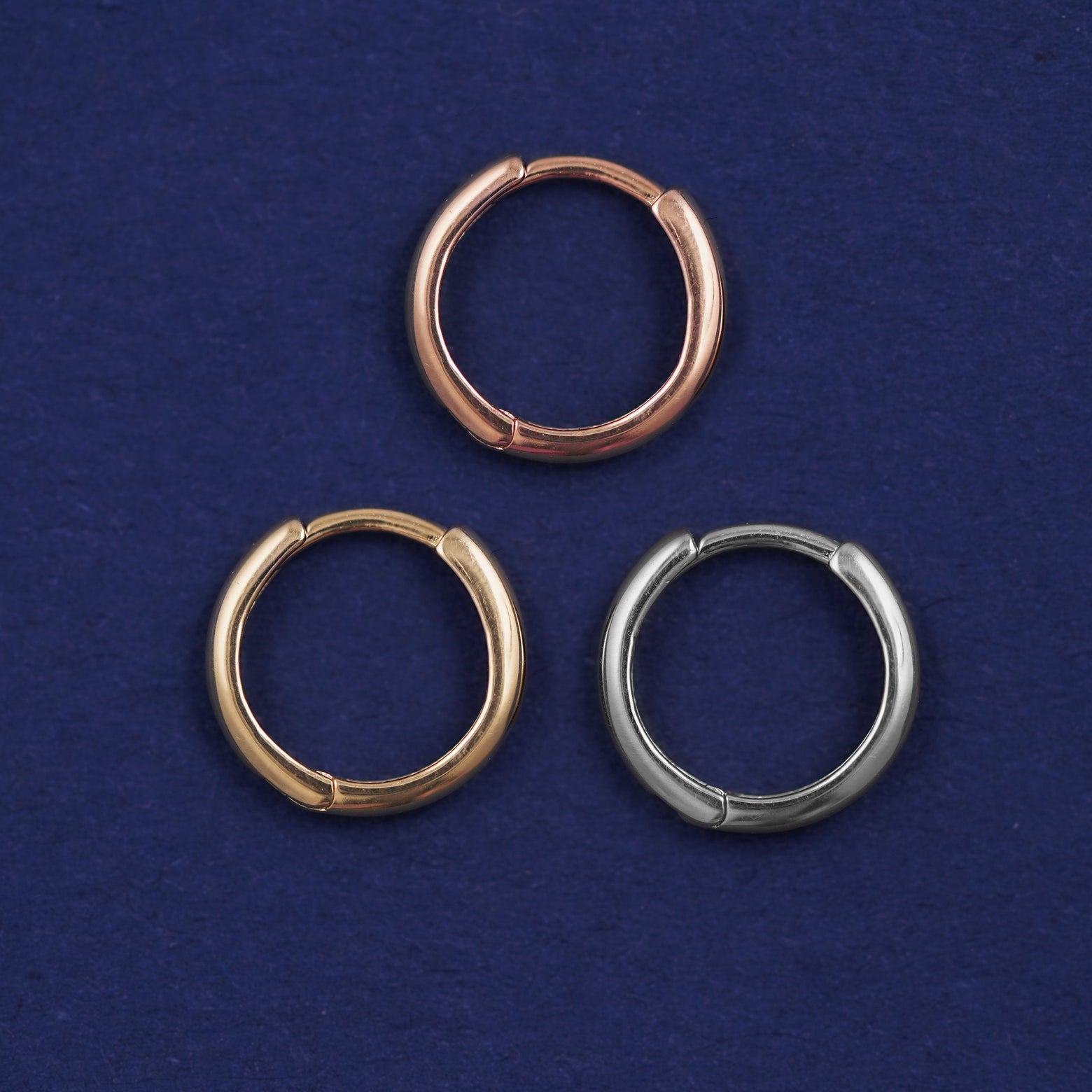 Three versions of the Small Curvy Huggie Hoop shown in options of rose, yellow, and white gold