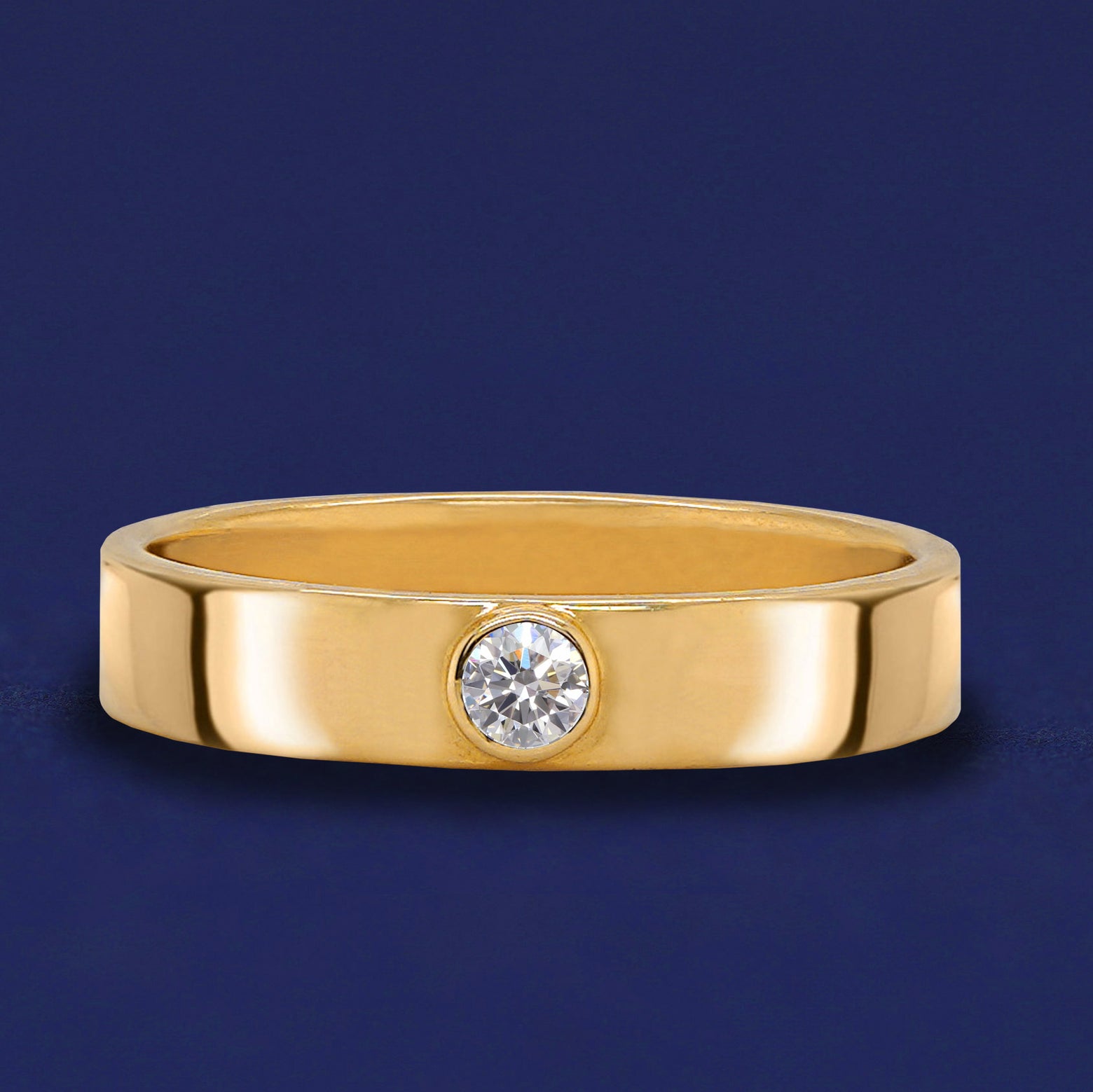 A 14 karat solid gold band ring with a bezel set Diamond on a dark blue background