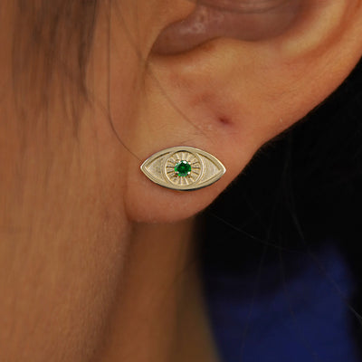 A model's ear wearing a yellow gold emerald Gemstone Evil Eye Earring