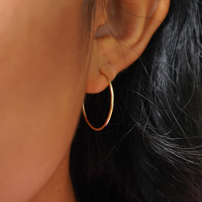 A model's ear wearing a solid 14k gold Medium Hoop