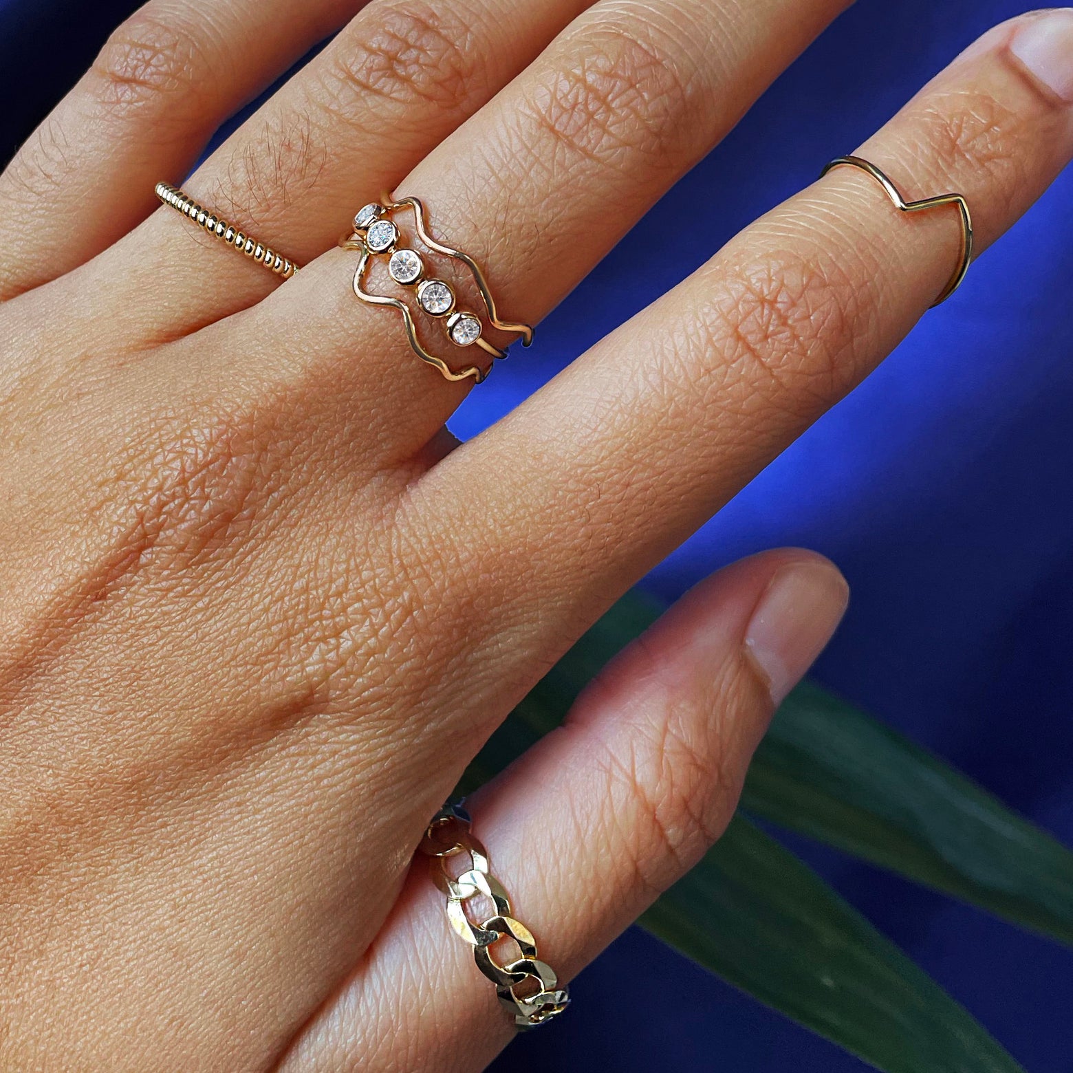 Close up view of a model's hand wearing a 5 diamond ring between two wave rings, a rope ring, and a curb ring
