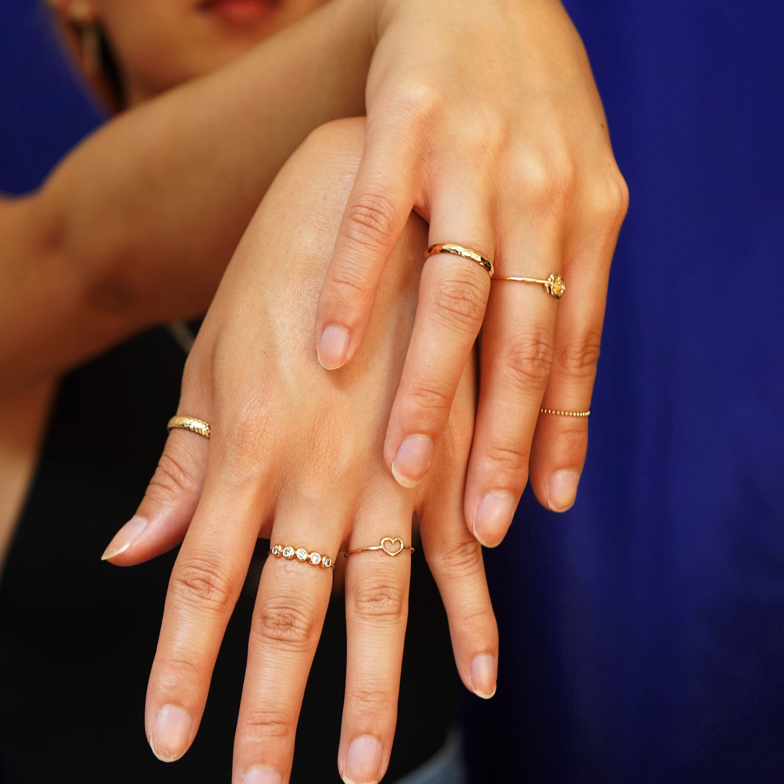 A model standing with their arms raised and hands crossed at the wrists while wearing various Automic Gold rings