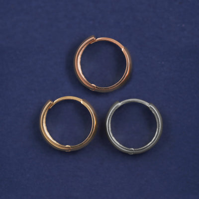 Three versions of the Medium Thick Huggie Hoop shown in options of rose, yellow, and white gold