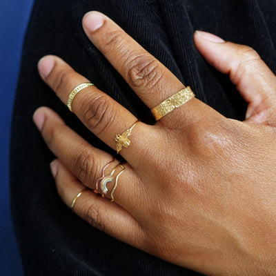 A model's hand resting on their shoulder while wearing stack of various Automic Gold rings
