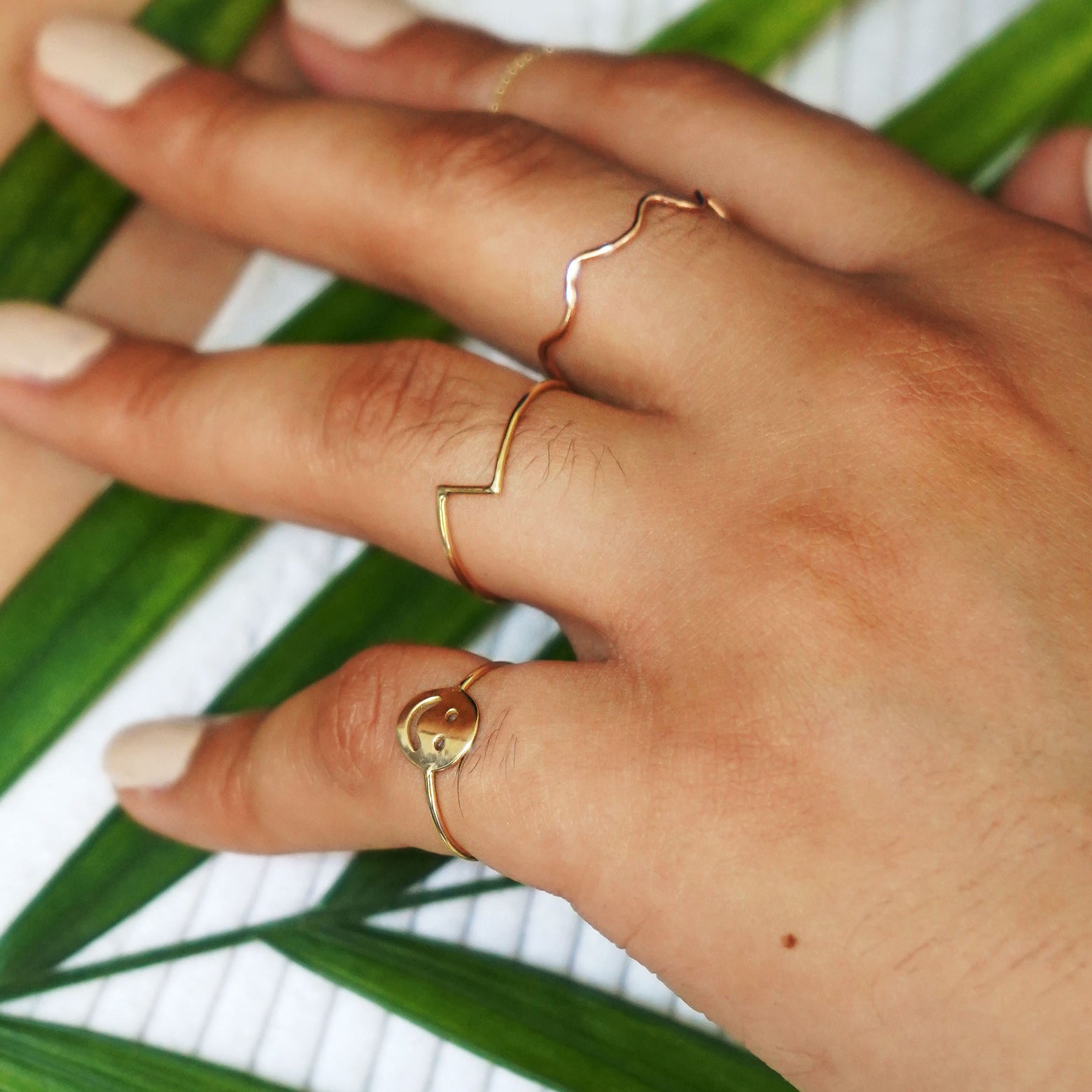 A model's hand on their chest holding a palm leaf wearing a Zig Zag Ring and other Automic Gold rings