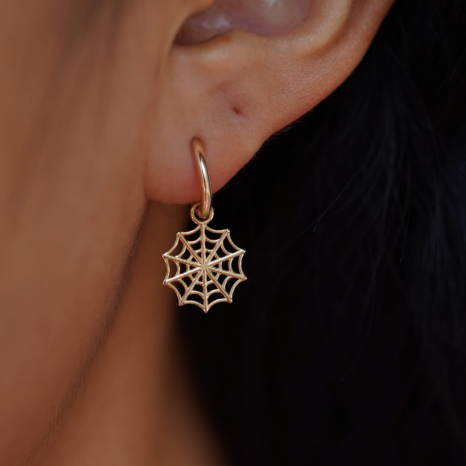 Close up view of a model's ear wearing a yellow gold Spider Web Charm on a Curvy Huggie Hoop