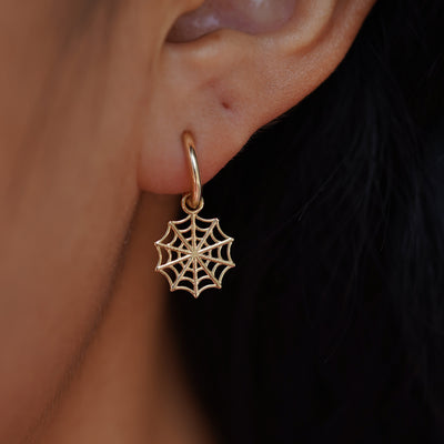 Close up view of a model's ear wearing a yellow gold Spider Web Charm on a Curvy Huggie Hoop