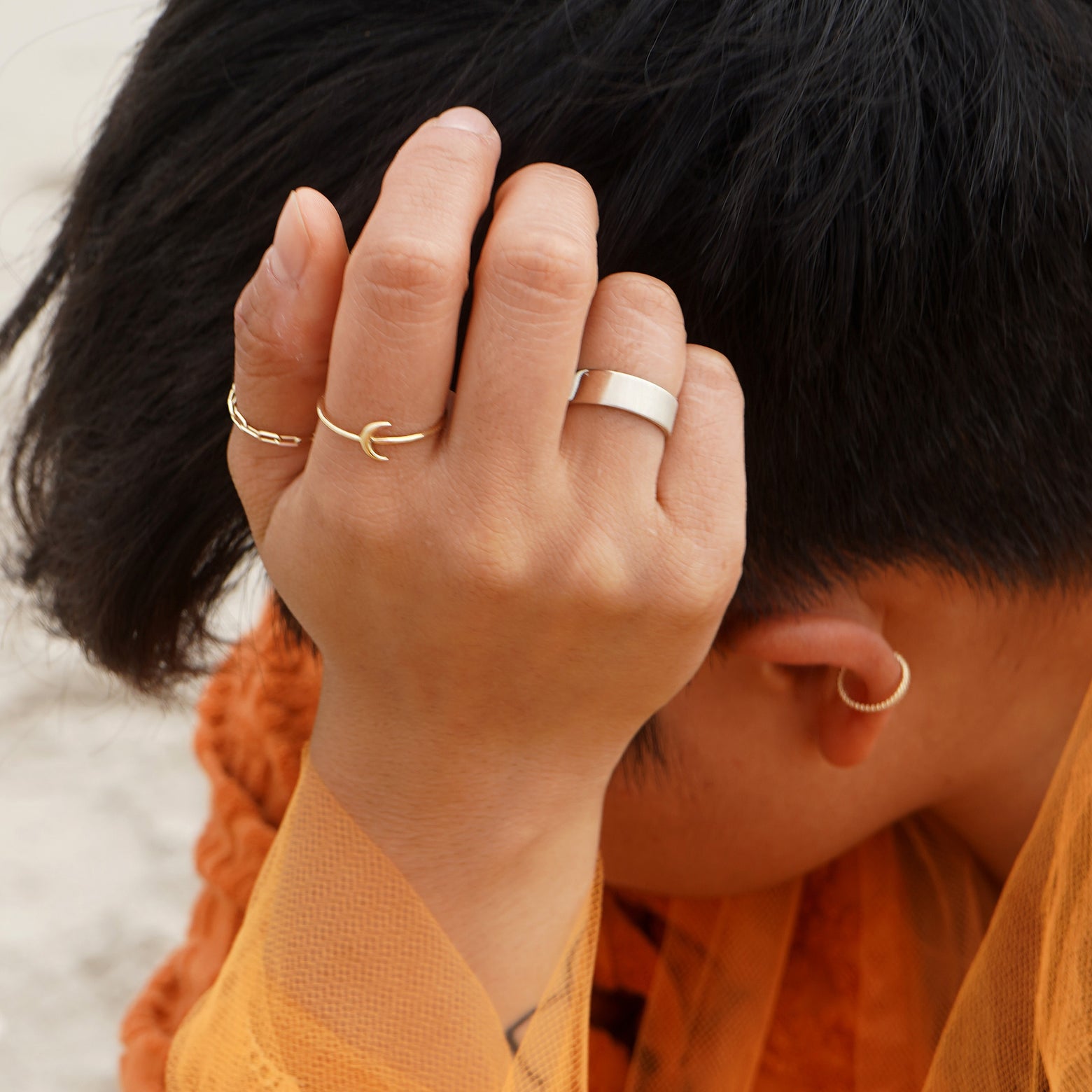 A model with their wrist resting against their temple wearing a Moon Ring and other Automic Gold rings