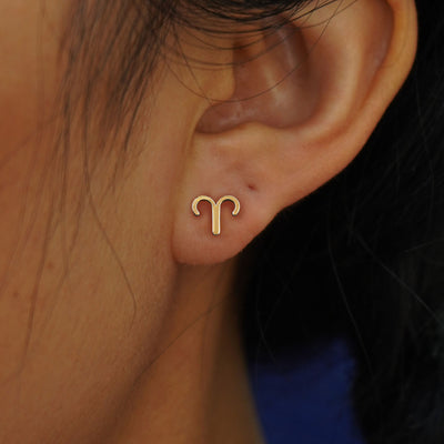A model's ear wearing a 14k yellow gold Horoscope Earring with an Aries zodiac symbol