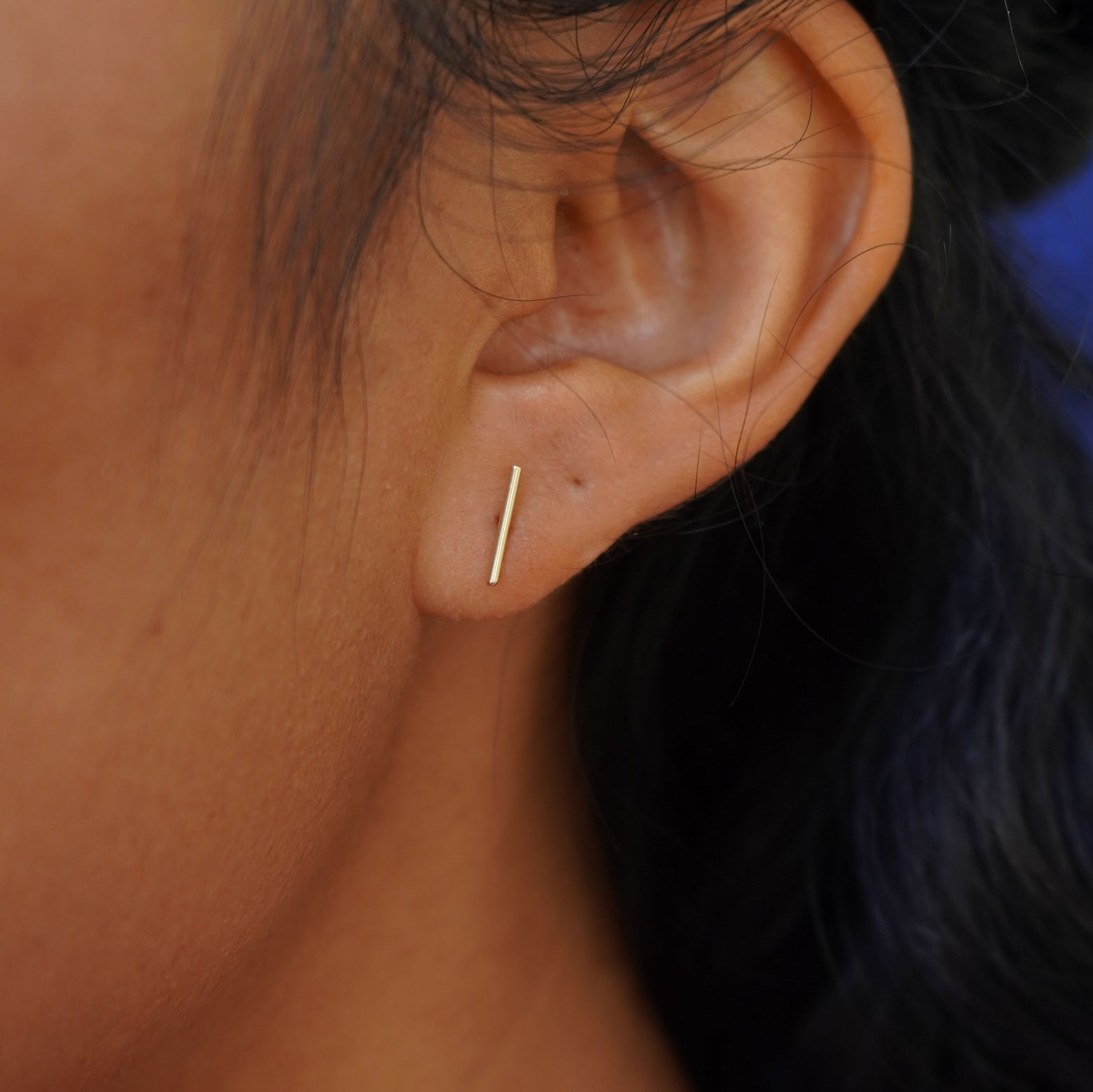 Close up view of a model's ear wearing a yellow gold Tall Line Earring