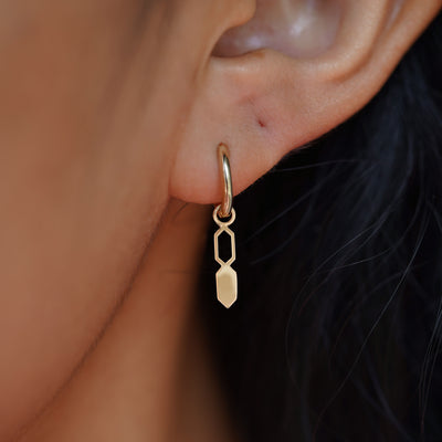 Close up view of a model's ear wearing a yellow gold Tanlah Charm on a Curvy Huggie Hoop