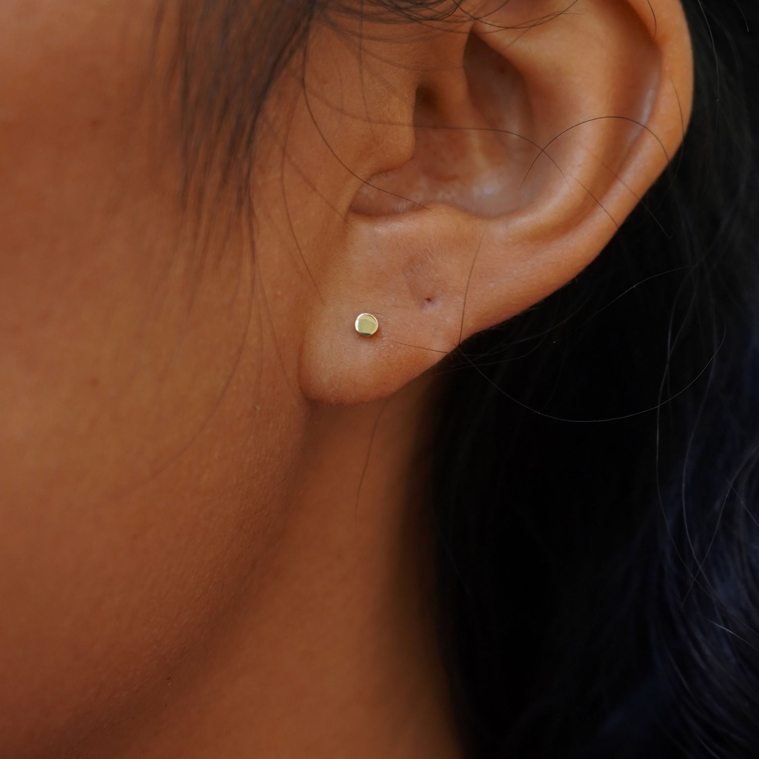 A model's ear wearing a 14k gold Teeny Tiny Circle Earring