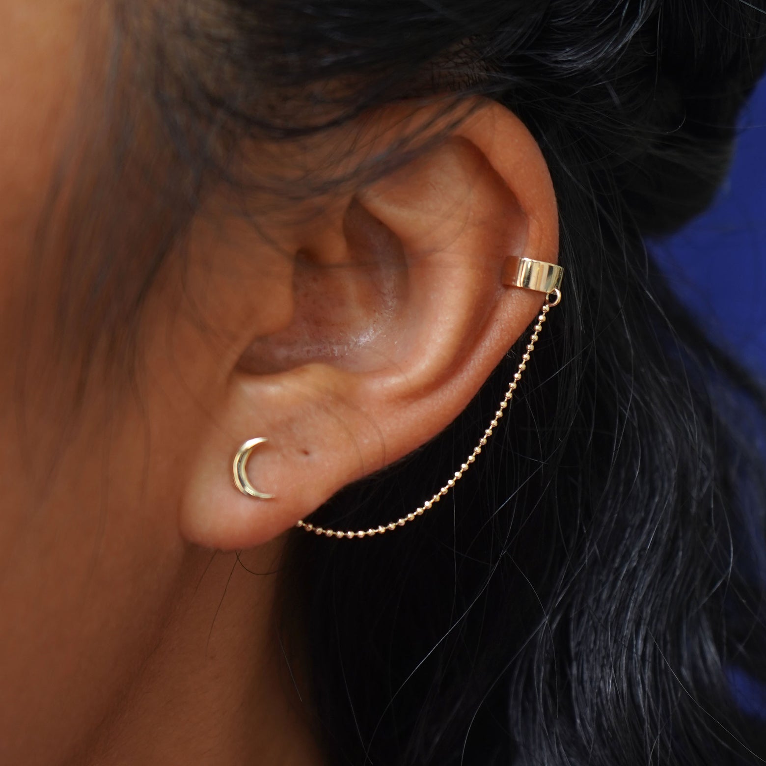 A model's ear wearing a yellow gold Thick Cuff With Chain and a Moon Earring