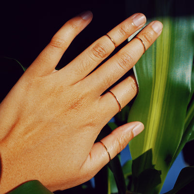 A model holding a plant leaf between two fingers while wearing a Line Ring on every finger except their pinky