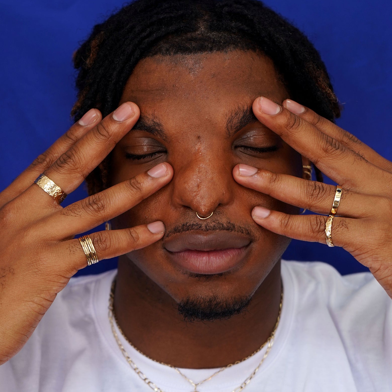A model posing with their fingers splayed against their face wearing a stack of Hammered Rings and various Automic Gold rings