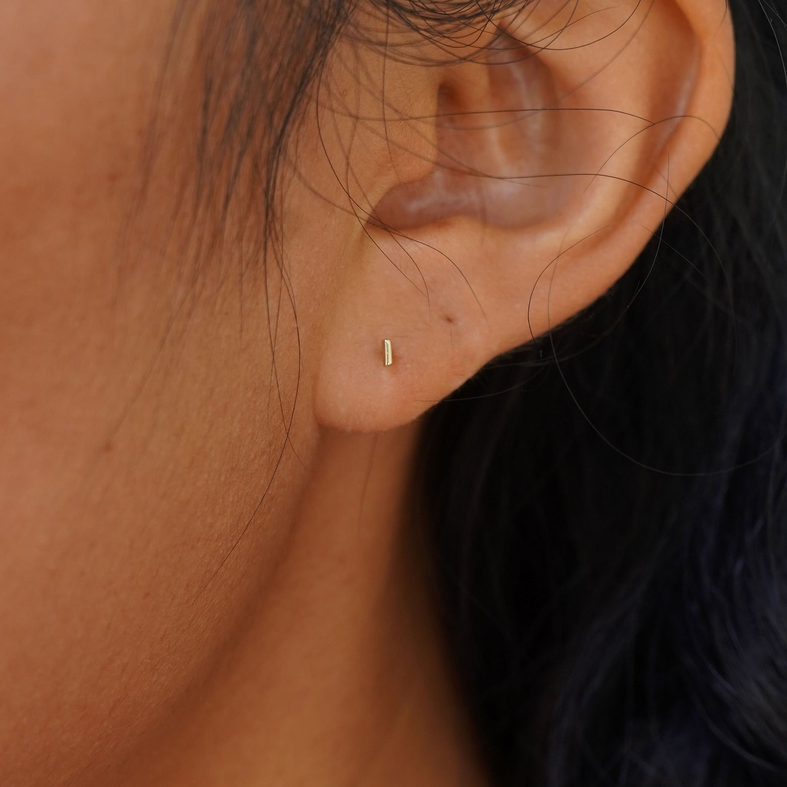 Close up view of a model's ear wearing a yellow gold Tiny Line Earring