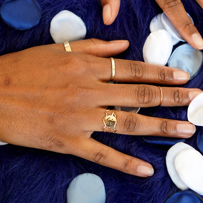 A model's hands touching blue and white flower petals while wearing Automic Gold rings
